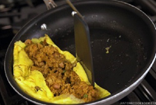 Bước 6: Cho cơm rang vào giữa, vun hai bên viền trứng, sau đó đổ ra đĩa, sao cho phần trứng ôm trọn lấy cơm. Cuối cùng cho cơm ra đĩa và đổ nước sốt lên trên.