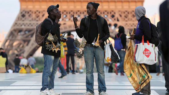 Hai thanh niên châu Phi đang bán mô hình tháp Eiffel dưới chân tháp Eiffel - Ảnh: LE PARISIEN
