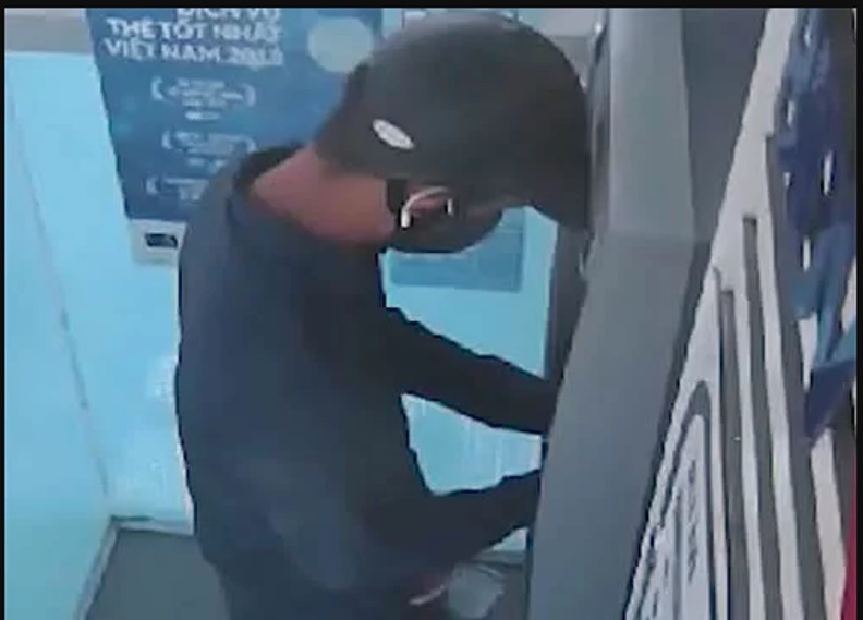 Người bịt mặt thực hiện hành vi đánh cắp dữ liệu tại cây ATM. Ảnh: Cắt từ video