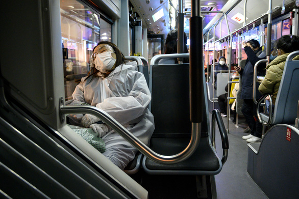 Một phụ nữ mang khẩu trang và áo mưa ngủ trên xe buýt ở Thượng Hải, Trung Quốc hôm 24-2 - Ảnh: AFP