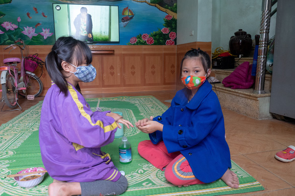 Hai chị em Hà Hồng Trang và Hà Thùy Linh - thôn Ngọc Bảo - rửa tay cho nhau bằng dung dịch sát khuẩn trong khi bố mẹ các em đi làm - Ảnh: VŨ TUẤN