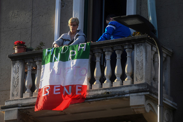 Một người dân tại thành phố Milan của Ý treo quốc kỳ bên ngoài ban công với dòng chữ "Mọi chuyện rồi sẽ ổn" - Ảnh: REUTERS