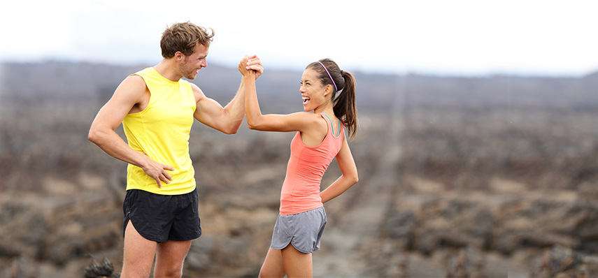 Fitness sport running couple celebrating cheerful and happy giving high five energetic and cheering. Runner couple having fun after trail cross-country running training. Asian woman, Caucasian man.