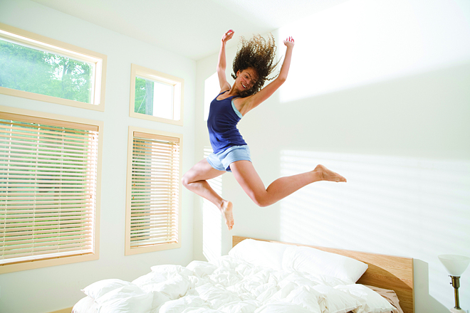 Attractive Young Woman Jumping Energetically on Bed