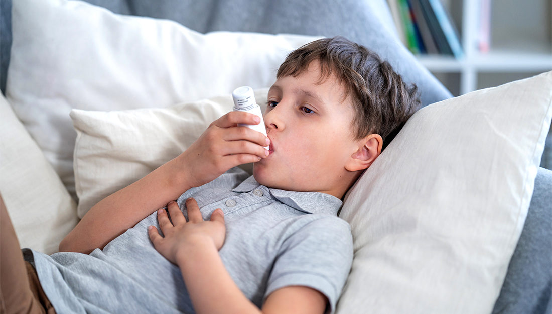 Sick boy tired from chest coughing holding inhaler, having asthma allergy using the asthma inhaler. Cough during the epidemic of SARS, Pneumonia and influenza. Child Coughs Lying In Bed.