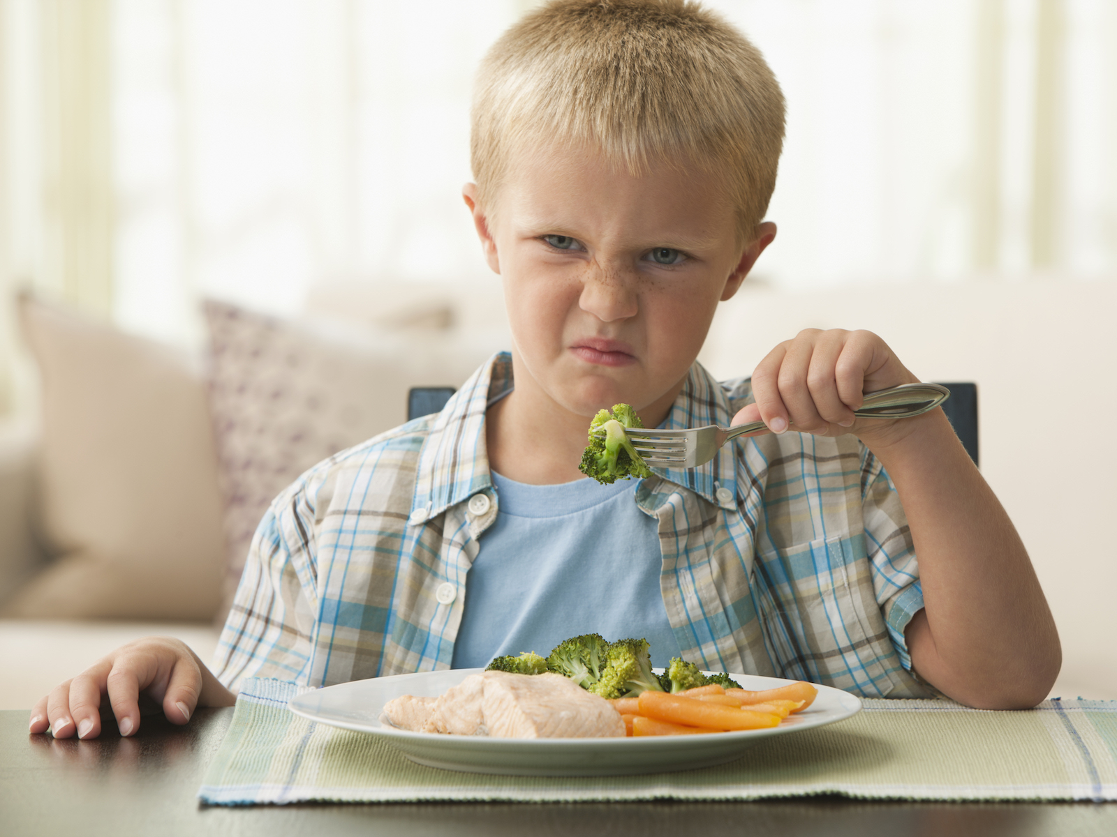 Unhappy Caucasian boy eating vegetables
