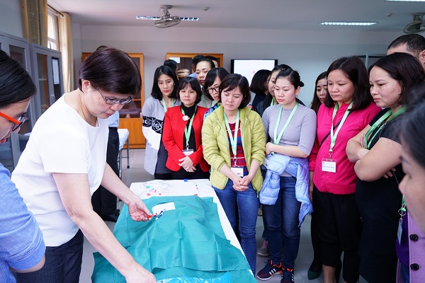 Bà Chan Siew Mie (trái, áo trắng), Tình nguyện viên Quốc tế Singapore và Quản lý y tá cấp cao từ Bệnh viện Tan Tock Seng đang thực hiện kỹ thuật đặt ống thông vĩnh viễn cho các Giảng viên nguồn của Việt Nam trong hội thảo đào tạo lâm sàng năm 2018. 